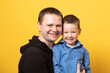 Happy father's day! Cute father and son hugging on yellow background. Portrait of a dad with a baby boy smiling and hugging. Family concept.