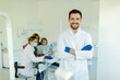 Male dentist standing with his hands crossed, wearing gloves and white coat and looking at camera.