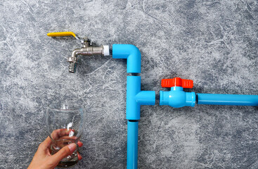 Blue PVC pipe with faucet and water valve with copy space. A glass of water in hand.