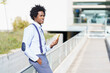 © javiindy - Black man with afro hairstyle using a smartphone near an office building.