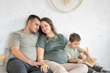 Happy family sitting at the bed. Parents and little boy. Boy reading a book. Candid family concept