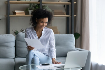 Happy young African American woman use computer pay household expenses expenditures online. Smiling biracial female manage family budget count finances, make payment on laptop. Banking concept.