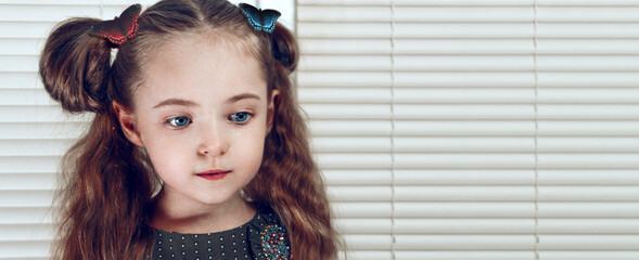 A baby girl looks away against the backdrop of the cream blinds. A great place for text. On the hair of butterflies of different colors, loose thick hair