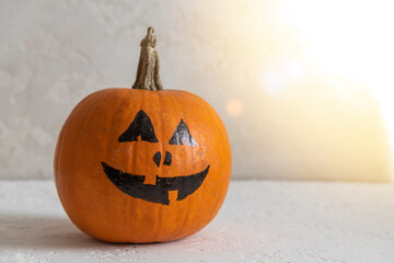 Wall Mural - Close-up view of orange Halloween pumpkin with black drawing face lying on white table. Jack O'Lantern. Side view. Homemade Halloween decoration theme.