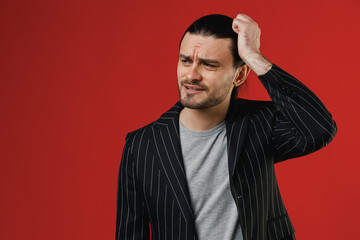 Young sad puzzled confused thoughtful businessman latin man 20s long hair ponytail wear black striped jacket grey shirt scratch head look aside isolated on red background. Concept of people lifestyle.