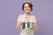 Young smiling happy satisfied fun housewife housekeeper chef cook baker woman in pink apron giving soup stainless pan saucepan isolated on pastel violet background studio Cooking food process concept
