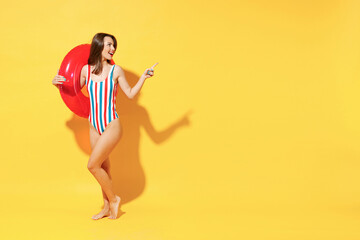 Wall Mural - Full length fun happy young sexy woman slim body wear red blue swimsuit pose go with inflatable rubber ring isolated on vivid yellow color background studio Summer hotel pool sea rest sun tan concept