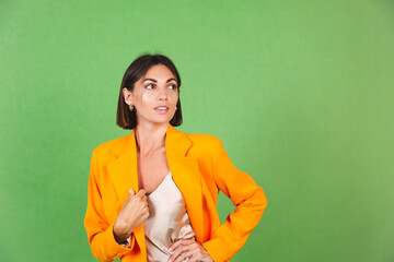 Wall Mural - Stylish woman in silk beige dress and orange oversized blazer on green background, positive emotions smile