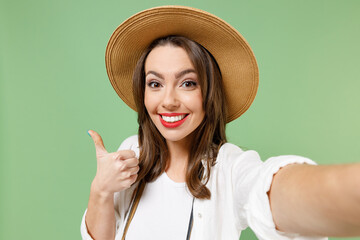 Close up traveler tourist woman in casual clothes hat camera do selfie shot on mobile phone show thumb up isolated on green background Passenger travel abroad on weekends. Air flight journey concept.