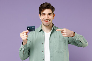 Wall Mural - Young smiling happy caucasian man 20s in casual mint shirt white t-shirt point index finger on credit bank card looking camera isolated on purple background studio portrait People lifestyle concept.