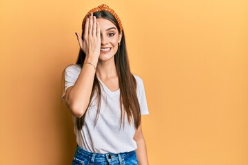 Wall Mural - Beautiful brunette young woman wearing casual white t shirt covering one eye with hand, confident smile on face and surprise emotion.