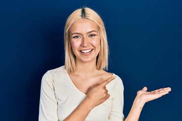 Poster - Beautiful blonde woman wearing casual sweater amazed and smiling to the camera while presenting with hand and pointing with finger.