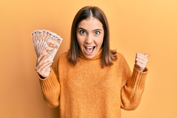 Sticker - Young blonde woman holding 50 turkish lira banknotes screaming proud, celebrating victory and success very excited with raised arm