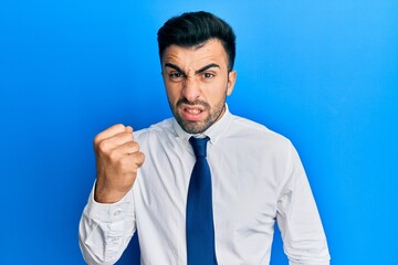 Wall Mural - Young hispanic man wearing business clothes angry and mad raising fist frustrated and furious while shouting with anger. rage and aggressive concept.