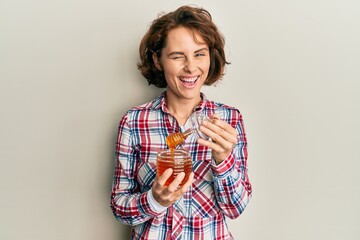 Poster - Young brunette woman holding fresh honey winking looking at the camera with sexy expression, cheerful and happy face.