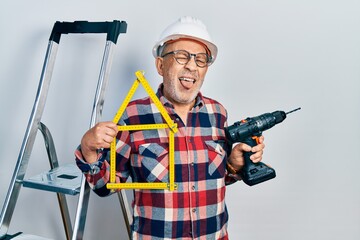 Sticker - Handsome mature handyman holding screwdriver wearing hardhat by construction stairs sticking tongue out happy with funny expression.