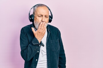 Wall Mural - Handsome senior man with beard listening to music using headphones bored yawning tired covering mouth with hand. restless and sleepiness.