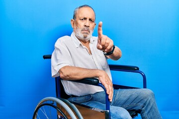 Sticker - Handsome senior man with beard sitting on wheelchair pointing with finger up and angry expression, showing no gesture