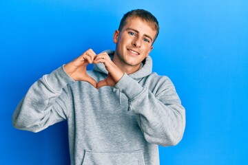 Young caucasian man wearing casual sweatshirt smiling in love doing heart symbol shape with hands. romantic concept.