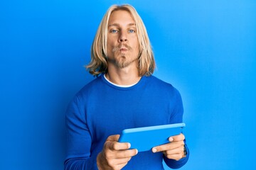 Canvas Print - Caucasian young man with long hair using touchpad device looking at the camera blowing a kiss being lovely and sexy. love expression.