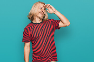 Canvas Print - Caucasian man with blond long hair wearing casual striped t shirt very happy and smiling looking far away with hand over head. searching concept.