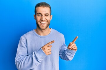 Canvas Print - Young caucasian man pointing with fingers to the side winking looking at the camera with sexy expression, cheerful and happy face.