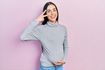 Canvas Print - Beautiful woman with blue eyes expecting a baby, touching pregnant belly doing peace symbol with fingers over face, smiling cheerful showing victory