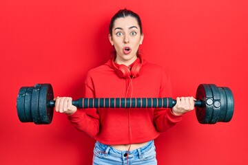 Sticker - Beautiful woman with blue eyes wearing sportswear using dumbbells afraid and shocked with surprise and amazed expression, fear and excited face.