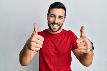 Young hispanic man wearing casual clothes approving doing positive gesture with hand, thumbs up smiling and happy for success. winner gesture.