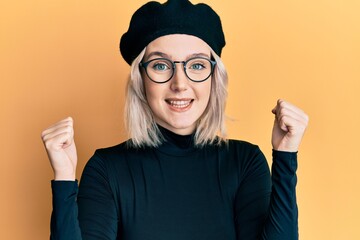 Poster - Young blonde girl wearing french look with beret celebrating surprised and amazed for success with arms raised and open eyes. winner concept.