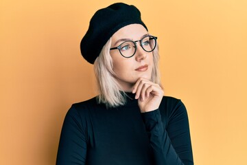 Poster - Young blonde girl wearing french look with beret with hand on chin thinking about question, pensive expression. smiling with thoughtful face. doubt concept.