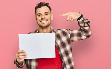 Canvas Print - Young hispanic man holding blank empty banner pointing finger to one self smiling happy and proud