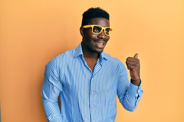 Wall Mural - Handsome black man wearing yellow glasses pointing thumb up to the side smiling happy with open mouth