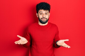 Poster - Young arab man with beard wearing casual red sweater clueless and confused expression with arms and hands raised. doubt concept.