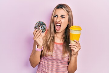 Sticker - Beautiful hispanic woman eating doughnut and drinking coffee angry and mad screaming frustrated and furious, shouting with anger. rage and aggressive concept.