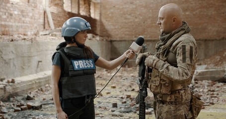 Sticker - POV Female war journalist correspondent wearing bulletproof vest and helmet reporting live near destroyed building, conducting interview with military representative