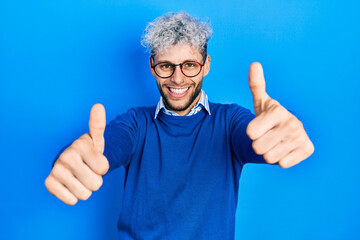 Young hispanic man with modern dyed hair wearing sweater and glasses approving doing positive gesture with hand, thumbs up smiling and happy for success. winner gesture.