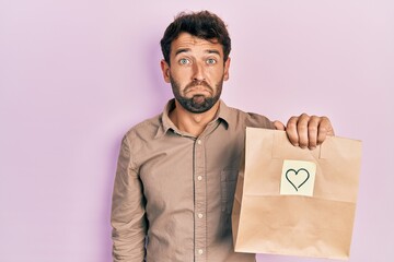 Sticker - Handsome man with beard holding delivery paper bag with heart reminder depressed and worry for distress, crying angry and afraid. sad expression.