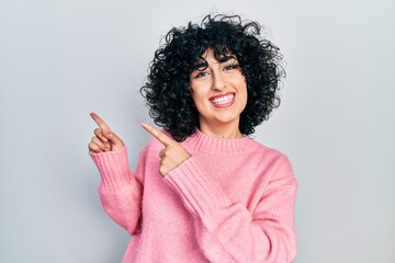 Poster - Young middle east woman wearing casual clothes smiling and looking at the camera pointing with two hands and fingers to the side.