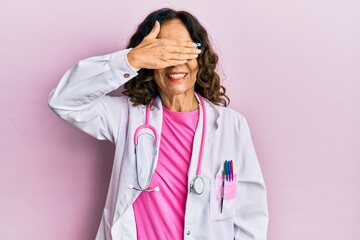 Poster - Middle age hispanic woman wearing doctor uniform and glasses smiling and laughing with hand on face covering eyes for surprise. blind concept.