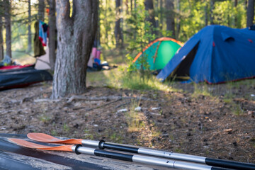 oars lie on an overturned kayak on the shore, in the camp, against the backdrop of a tent and forest