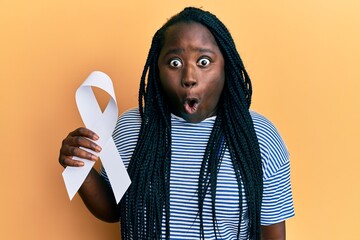 Wall Mural - Young black woman with braids holding white ribbon scared and amazed with open mouth for surprise, disbelief face