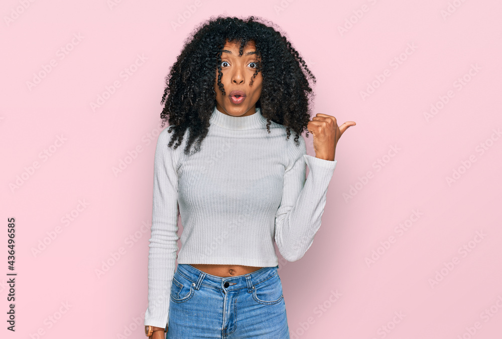 Young african american girl wearing casual clothes surprised pointing with hand finger to the side, open mouth amazed expression. - obrazy, fototapety, plakaty 