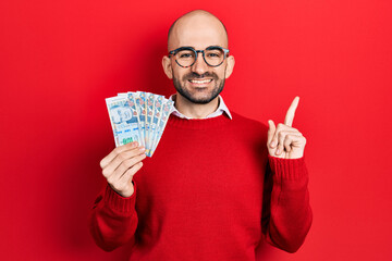 Sticker - Young bald man holding peruvian sol banknotes smiling happy pointing with hand and finger to the side