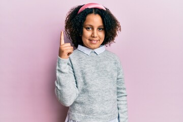 Sticker - Young little girl with afro hair wearing casual clothes pointing finger up with successful idea. exited and happy. number one.