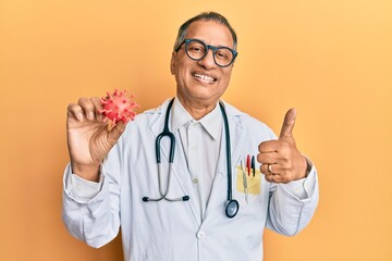 Sticker - Middle age indian man wearing doctor coat holding virus toy smiling happy and positive, thumb up doing excellent and approval sign