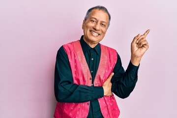 Sticker - Middle age indian man wearing traditional indian clothes with a big smile on face, pointing with hand and finger to the side looking at the camera.