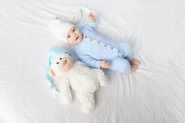 Wall Mural - happy baby on the bed in a hood. Textiles and bedding for children. Newborn baby with a toy bear