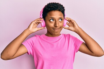 Wall Mural - Young african american girl listening to music using headphones smiling looking to the side and staring away thinking.