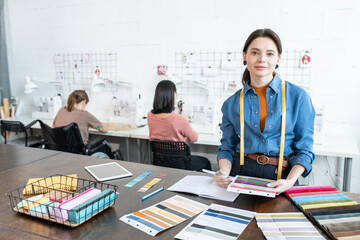 Poster - Pretty female fashion designer working against seamstresses